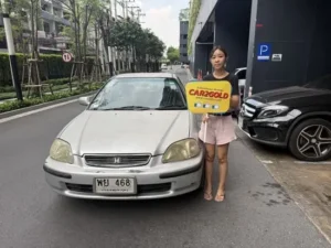 ภาพรีวิวรับซื้อรถบ้าน ลูกค้ายืนถือป้าย CAR2GOLD หน้าป้ายทะเบียนรถ Honda Civic โฉมตาโต (EK)