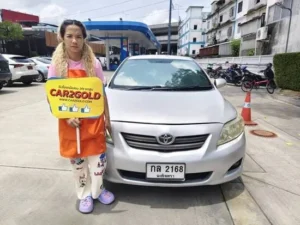 ภาพรีวิวรับซื้อรถเก่า Toyota Corolla Altis โฉมหน้าแบน (E140) ลูกค้ายืนถือป้ายการันตี CAR2GOLD